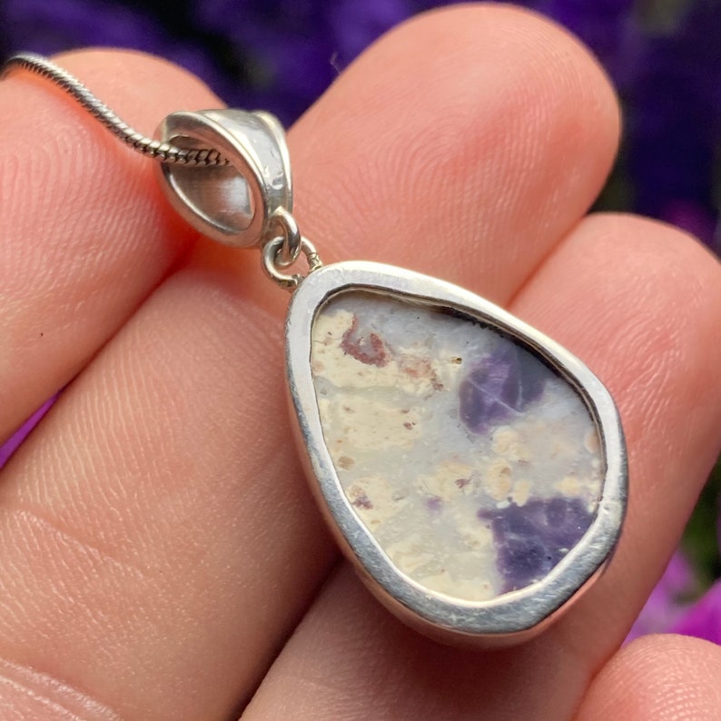 May include: A silver pendant with a teardrop-shaped opal stone. The opal has a white base with purple and brown inclusions.