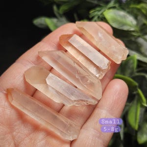 May include: Four translucent, light orange-tinted quartz crystal points with pointed terminations and natural facets. A purple rectangular label in the corner displays the text "Small 5-8g" indicating the weight range for these mineral specimens.