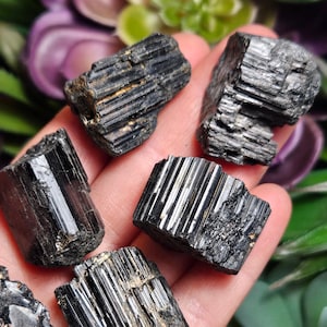 Peut inclure: Cinq cristaux de tourmaline noire brute pr&eacute;sentant des stries verticales distinctes et une texture de surface sombre et brillante. Ces pierres pr&eacute;sentent des bords naturels irr&eacute;guliers et une structure colonnaire typique du min&eacute;ral.