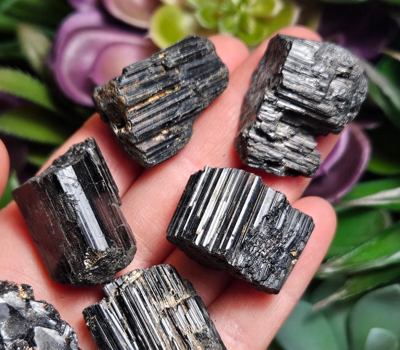 Peut inclure: Cinq cristaux de tourmaline noire brute pr&eacute;sentant des stries verticales distinctes et une texture de surface sombre et brillante. Ces pierres pr&eacute;sentent des bords naturels irr&eacute;guliers et une structure colonnaire typique du min&eacute;ral.