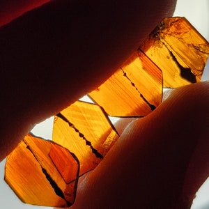 May include: A collection of four translucent, amber-colored, faceted crystals with striations. The crystals are arranged in a fan shape, with the largest crystal at the top and the smallest crystal at the bottom.
