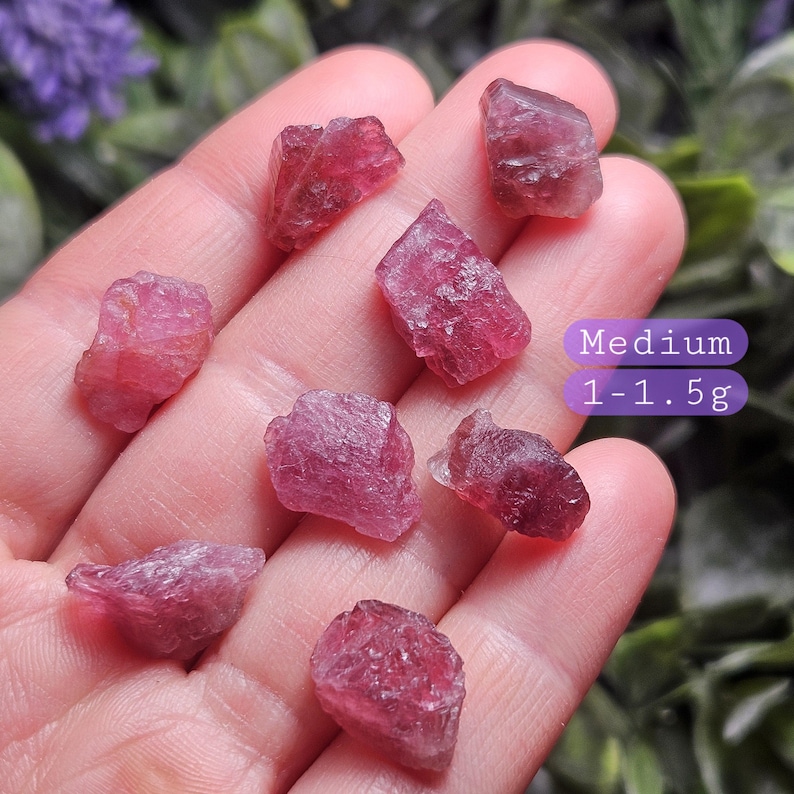 May include: Several raw, deep pink tourmaline crystals with irregular, faceted surfaces. A purple text overlay on the right side reads Medium 1-1.5g, indicating the weight range for these small, translucent, and naturally textured mineral stones.