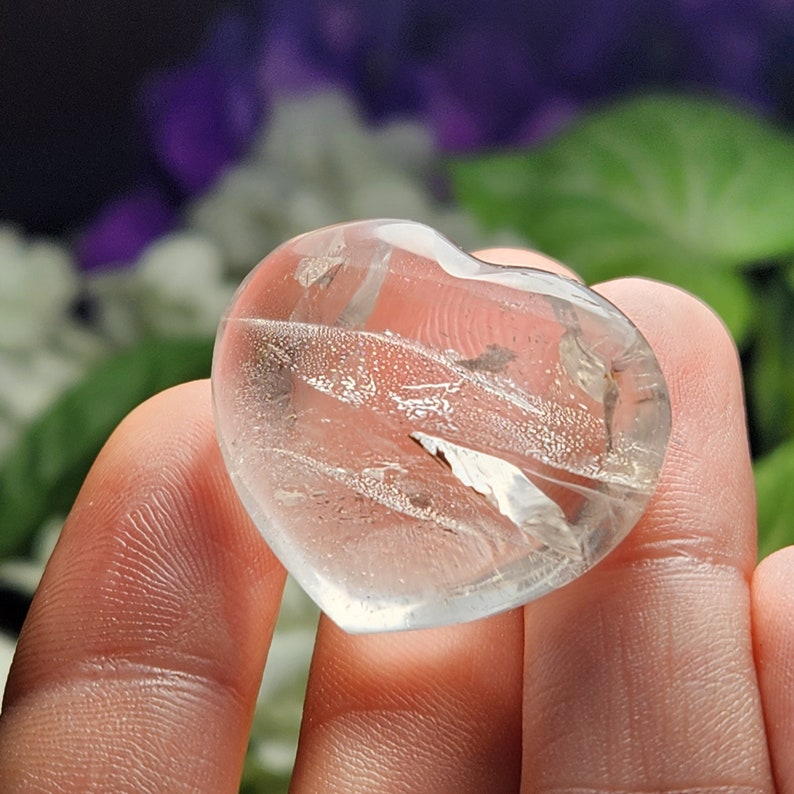 May include: A clear quartz heart with a natural, cloudy, and striated texture. The heart is polished and smooth.