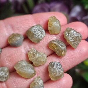Puede incluir: Una colecci&oacute;n de gemas en bruto, sin cortar, en tonos amarillo p&aacute;lido y gris. Las piedras tienen una superficie rugosa y texturizada, con formas irregulares. Las gemas se muestran sobre un fondo borroso.