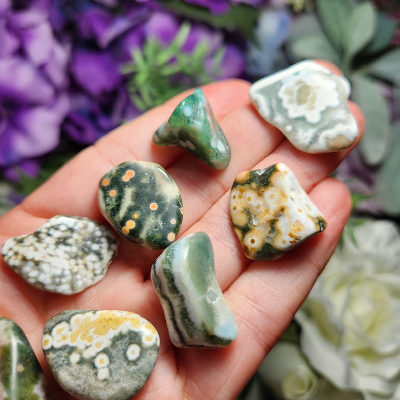 May include: A collection of seven green, white, and brown ocean jasper tumbled stones. The stones have a variety of patterns and shapes.