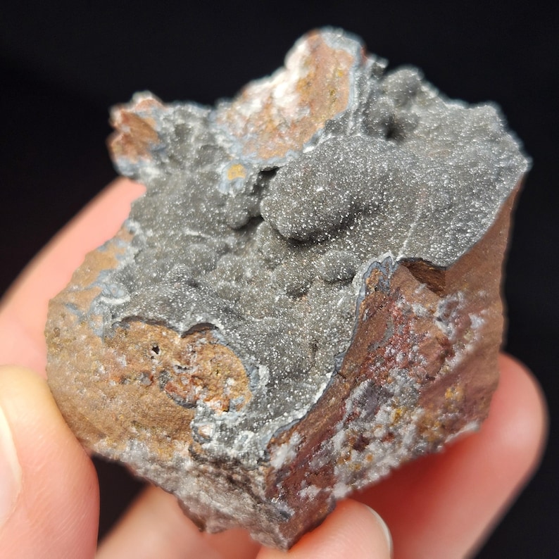 May include: A close-up of a mineral specimen with a rough, textured surface. The rock features a mix of colors, including gray, brown, and reddish-brown. The gray portion has a granular appearance, while the brown areas show a layered structure.