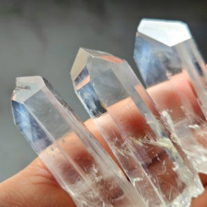 May include: Three clear quartz crystal points with a slightly cloudy appearance. The crystals are pointed at the top and have a smooth, polished finish.