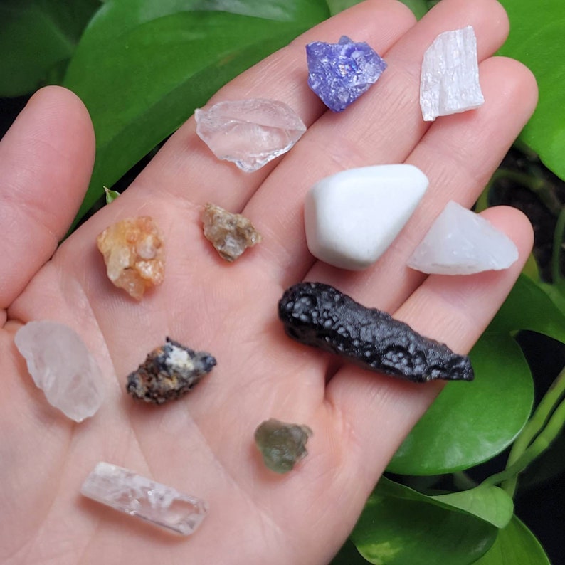 Puede incluir: Una colecci&oacute;n de varias piedras preciosas en tonos claros, blancos, naranjas, marrones, morados y negros. Las piedras preciosas son de diferentes formas y tama&ntilde;os, incluyendo un cristal claro y rectangular y una piedra blanca y redondeada.