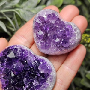 May include: Two amethyst heart-shaped crystal clusters with a purple and white color scheme. The crystals are clustered together in a natural formation.