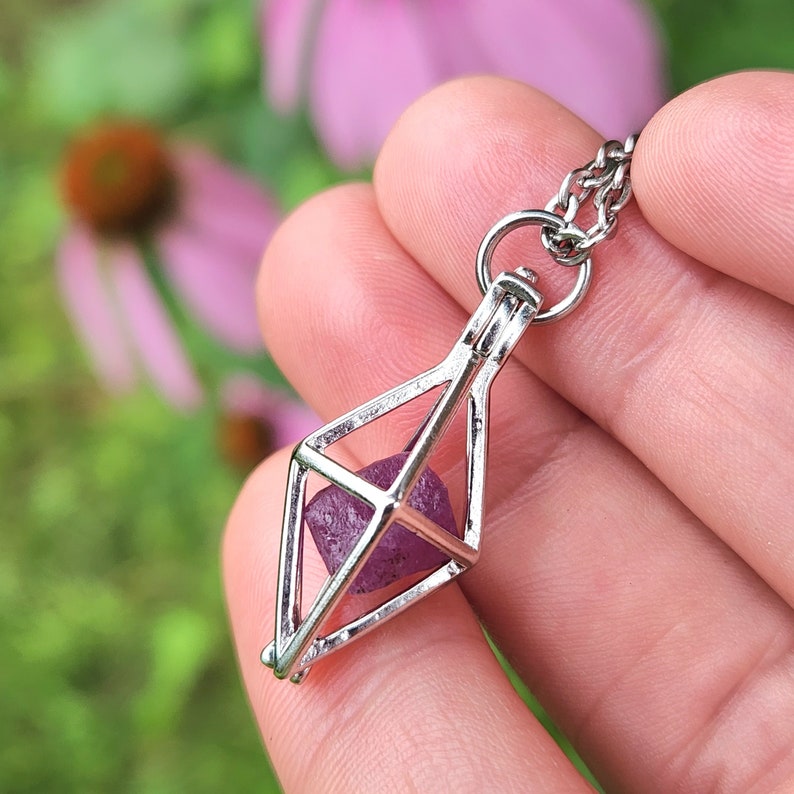 May include: A silver cage pendant necklace with a purple crystal inside. The cage is shaped like a diamond and has a delicate chain.