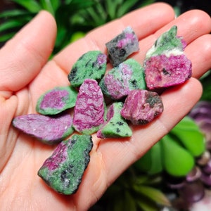 Pu&ograve; includere: Una manciata di pietre di rubino grezzo in zoisite. Le pietre mostrano un mix di colori, tra cui verde vibrante, magenta intenso e nero. La consistenza ruvida e naturale delle pietre &egrave; visibile, mostrando la loro forma organica. Queste pietre preziose sono ideali per la creazione di gioielli o la collezione.