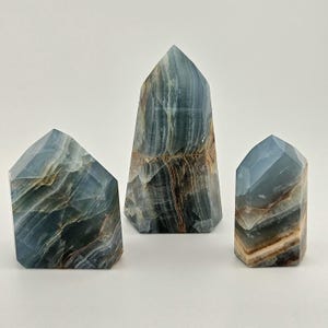 May include: Three blue calcite obelisks with brown and white veining. The obelisks are different sizes and have a faceted, geometric shape. The tallest obelisk is in the centre, with the other two on either side.