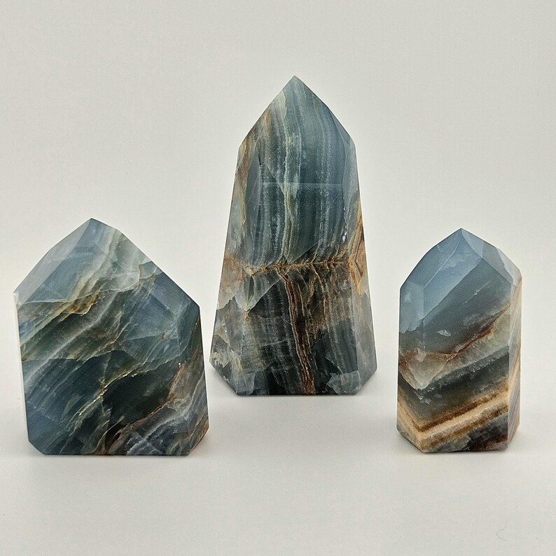 May include: Three blue calcite obelisks with brown and white veining. The obelisks are different sizes and have a faceted, geometric shape. The tallest obelisk is in the centre, with the other two on either side.