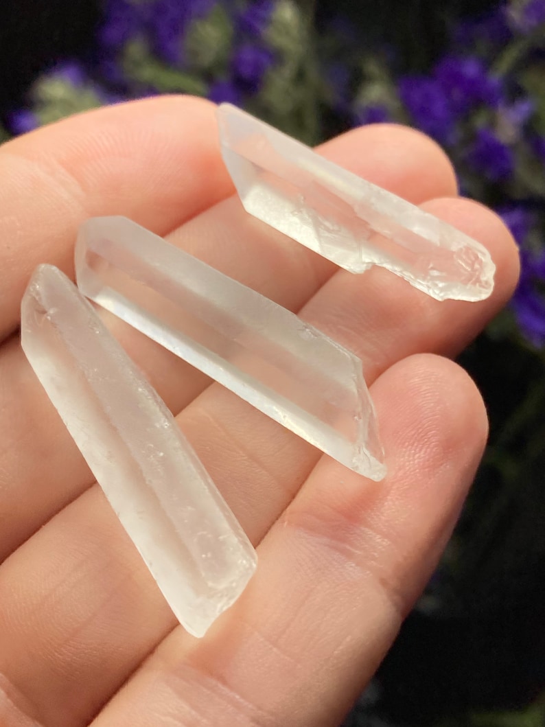 May include: Three clear quartz crystal points, also known as rock crystals, are displayed on a hand. The crystals are smooth and translucent.