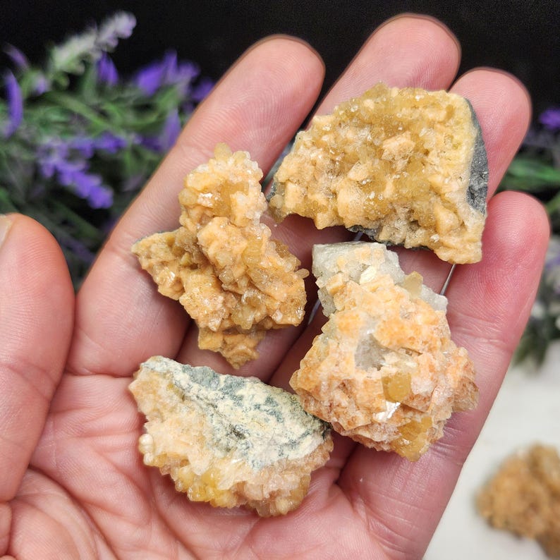 May include: A collection of raw, unpolished mineral specimens. The stones display a range of colors, including pale yellow, orange, and hints of green. The rough texture and natural formations are clearly visible, showcasing the mineral's crystalline structure.