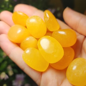 May include: A handful of smooth, polished yellow gemstones. The stones vary in size and shape, with an oval or teardrop form. The color is a vibrant, sunny yellow, and the stones appear to be translucent.