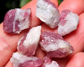 May include: A selection of raw tourmaline crystals, displaying a combination of pink and white colours. The crystals have a rough, natural texture, with the pink areas appearing more opaque and the white sections translucent. The image highlights the natural beauty of the gemstones.