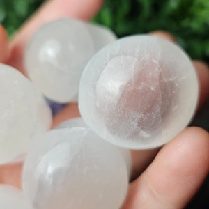 May include: A collection of smooth, white selenite tumbled stones. The stones are polished and have a translucent appearance.