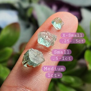 May include: Three green aquamarine crystals of varying sizes. The smallest crystal is labeled "X-Small .25-.5ct", the middle crystal is labeled "Small .5-1ct", and the largest crystal is labeled "Medium 1ct+".