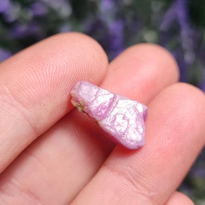May include: A pink and white rough cut gemstone with a natural, irregular shape. The gemstone has a shiny, iridescent surface.