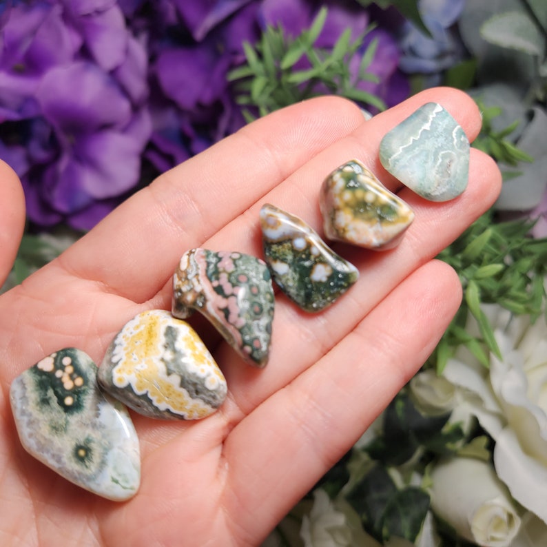 May include: A collection of six polished ocean jasper stones in various shades of green, brown, white, and pink. The stones are smooth and have a unique, swirling pattern.