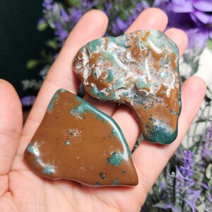 May include: Two green and brown polished stones with a rough, natural texture. The stones are irregularly shaped and have a mottled appearance.