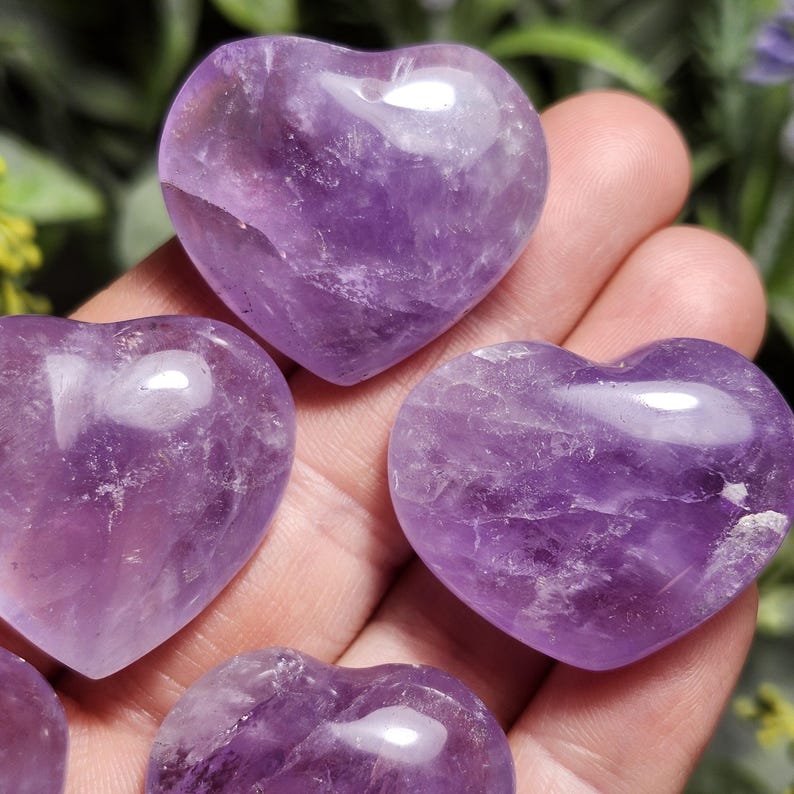 Puede incluir: Cinco cristales de amatista pulidos en forma de coraz&oacute;n. Los cristales son de color morado oscuro y tienen un acabado liso y pulido.