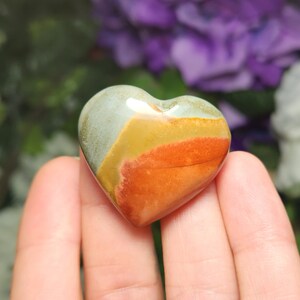 May include: A heart-shaped polished stone with layers of green, yellow, orange, and red colors.