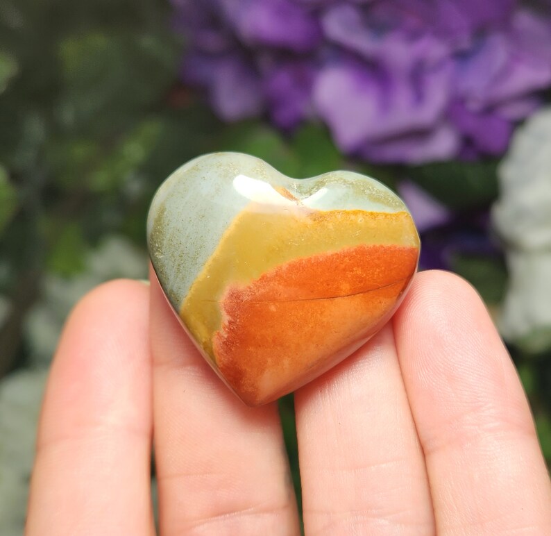May include: A heart-shaped polished stone with layers of green, yellow, orange, and red colors.