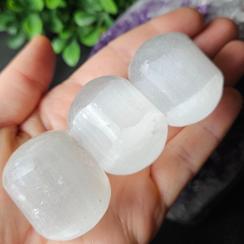 May include: Three white selenite tumbled stones, each with a smooth, rounded surface and a striated texture.
