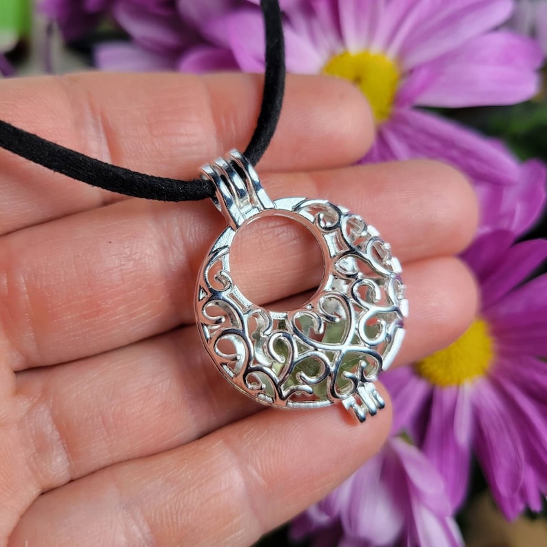 May include: A silver locket necklace with a delicate filigree design. The locket is open and has a small green stone inside.