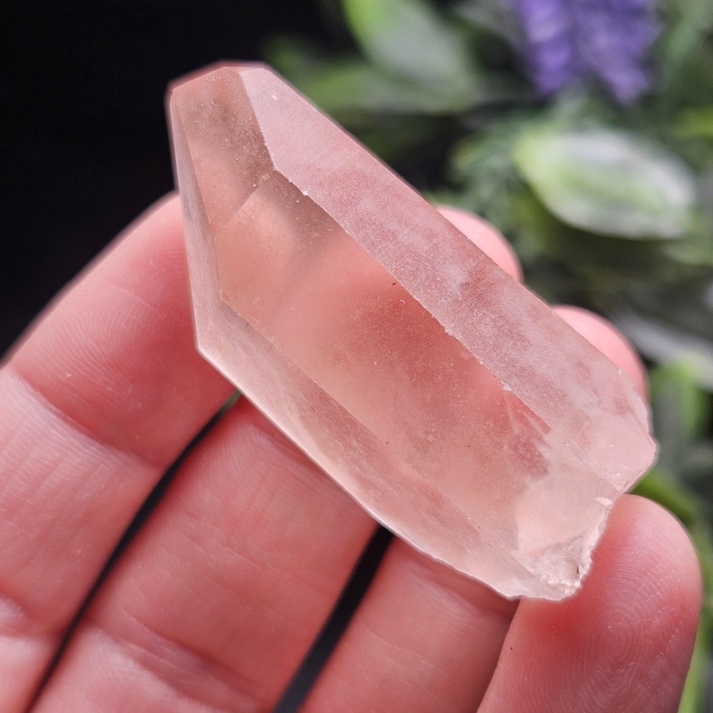 May include: A translucent, pale pink crystal point with a smooth, faceted surface and a pointed termination. The mineral displays a soft, light-reflecting quality with subtle internal inclusions visible throughout its elongated, hexagonal structure.