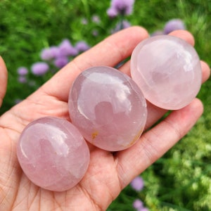 K&ouml;nnte beinhalten: Drei glatte, polierte Rosenquarzsteine mit einem durchscheinenden, blassrosa Farbton. Jeder Stein hat eine abgerundete, ovale Form mit einer gl&auml;nzenden, reflektierenden Oberfl&auml;che. Die Steine variieren leicht in der Gr&ouml;&szlig;e und weisen nat&uuml;rliche Einschl&uuml;sse auf.