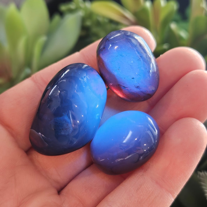 May include: Three smooth, oval-shaped blue and purple iridescent stones. The stones are translucent and have a slight shimmer.