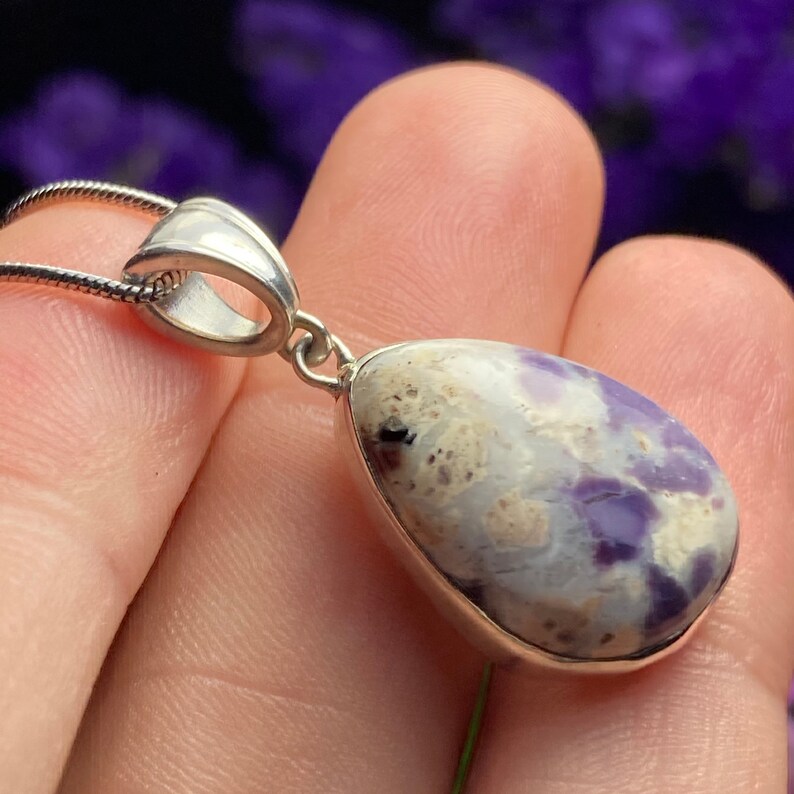 May include: A silver pendant featuring a teardrop-shaped purple and white stone with a silver bail.