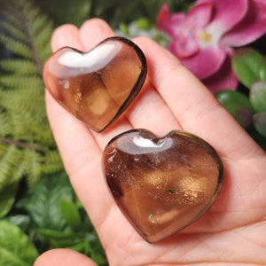 Puede incluir: Dos cristales de cuarzo ahumado en forma de coraz&oacute;n con un brillo dorado. Los cristales son transl&uacute;cidos y tienen un aspecto natural y en bruto.