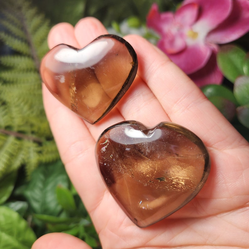 Puede incluir: Dos cristales de cuarzo ahumado en forma de coraz&oacute;n con un brillo dorado. Los cristales son transl&uacute;cidos y tienen un aspecto natural y en bruto.