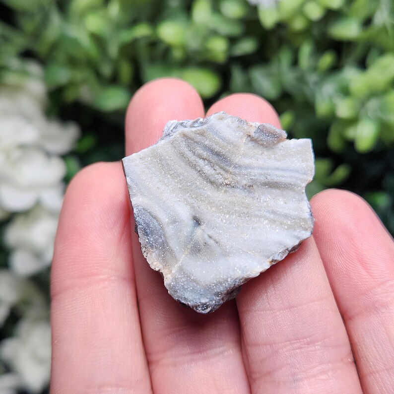 May include: A close-up of a white and gray banded agate crystal with a rough, natural texture. The crystal is translucent and has a slight shimmer.