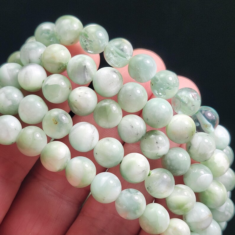 Peut inclure: Gros plan de plusieurs bracelets de perles de pierres pr&eacute;cieuses vert clair. Les perles rondes ont un aspect marbr&eacute; avec des variations de couleur. Les bracelets sont tenus dans une main sur fond sombre.