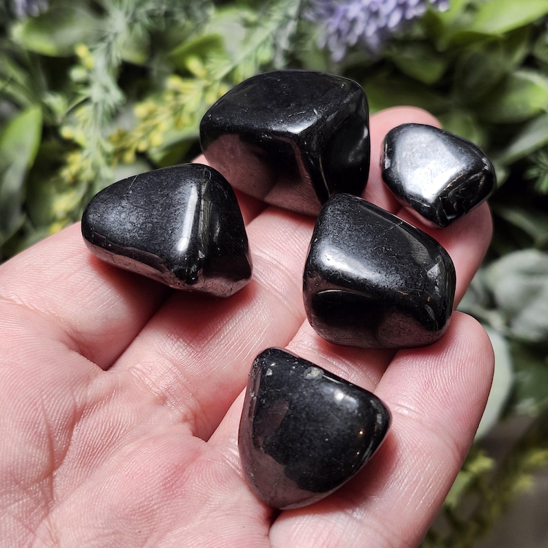 May include: Five smooth, black tumbled stones. The stones are various shapes and sizes, and have a glossy finish.