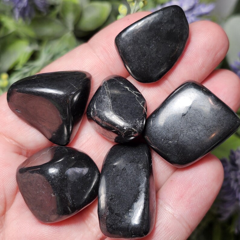May include: Six smooth, black tumbled stones. The stones are various shapes and sizes, and have a glossy finish.