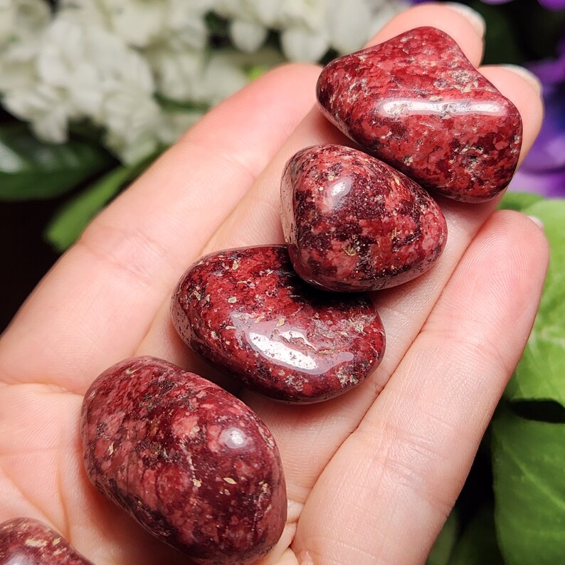 May include: Five tumbled red jasper stones with a speckled pattern. The stones are smooth and polished.