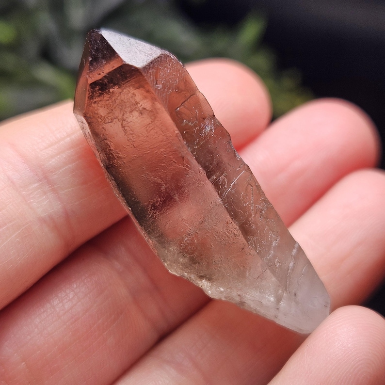 Puede incluir: Un cristal transl&uacute;cido de color marr&oacute;n con una punta afilada. El cristal tiene una textura natural y rugosa y un degradado de color, que va de un marr&oacute;n m&aacute;s oscuro en la parte superior a un tono m&aacute;s claro, casi transparente en la base. El cristal se sostiene en una mano.