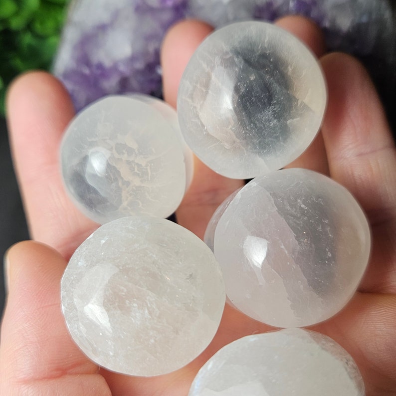 May include: Five smooth, white selenite spheres, each with a slightly different texture and translucence, are displayed on a hand. The spheres are approximately 2.5-5 cm in diameter.