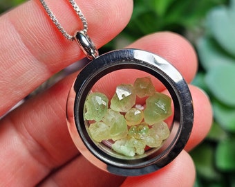 May include: A silver locket necklace with a clear glass insert containing a cluster of small, light green gemstones.
