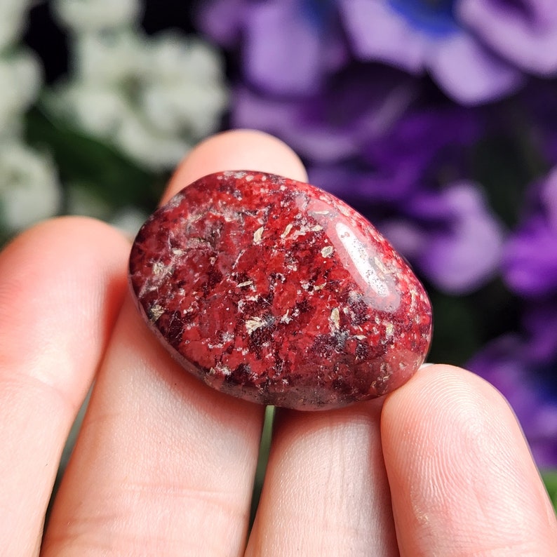 May include: A smooth, red and white tumbled stone with a speckled pattern.