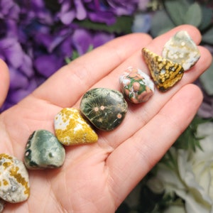 May include: A collection of seven polished ocean jasper stones in various shades of green, brown, and white with pink and orange accents. The stones are smooth and have a natural, organic look.