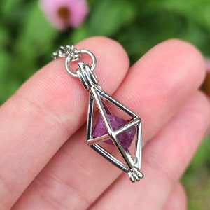 May include: A silver geometric cage pendant necklace with a small, faceted, purple gemstone inside.