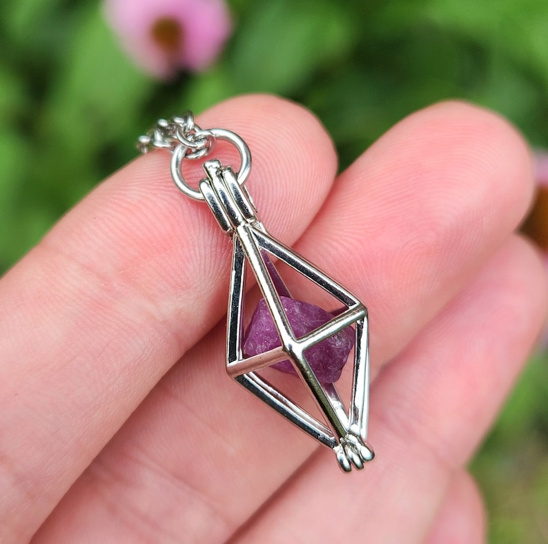 May include: A silver geometric cage pendant necklace with a small, faceted, purple gemstone inside.