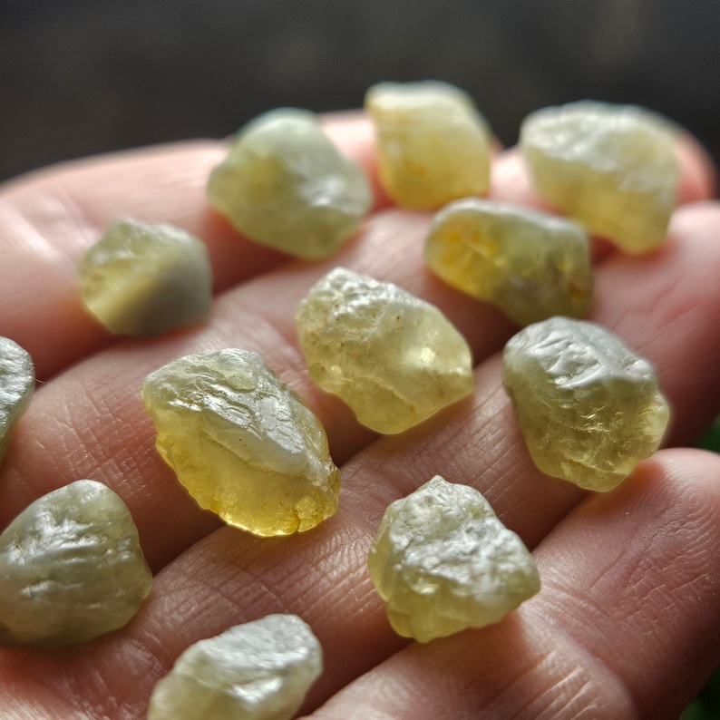 Puede incluir: Una colecci&oacute;n de piedras preciosas en bruto, sin cortar, en tonos amarillo p&aacute;lido y verde. Las piedras, de forma irregular, parecen transl&uacute;cidas y tienen una textura ligeramente rugosa. Las piedras preciosas se sostienen en una mano.